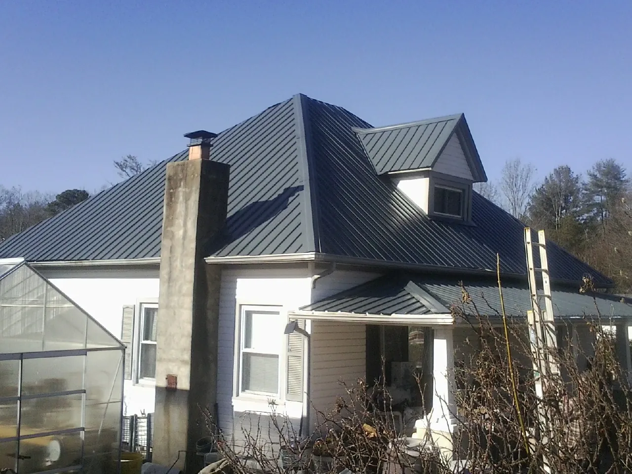 Dark blue standing seam metal roof on a white farmhouse with dormer — Slate & Tile Roof Repair by Roofing Brothers in Nelsonia