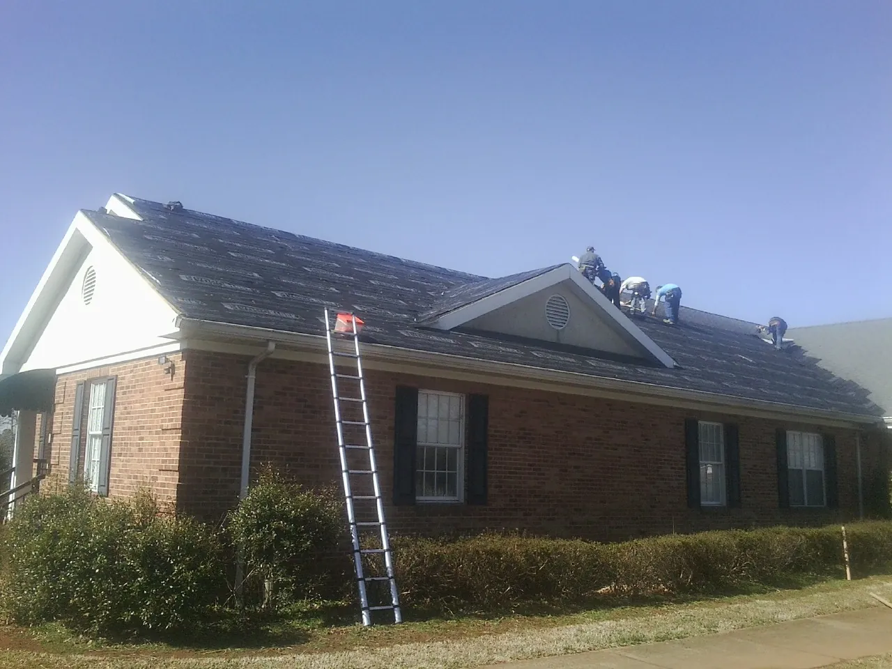 Crew tearing shingles off a brick ranch roof with a ladder set — Emergency Roof Repair work by our crew in Nelsonia