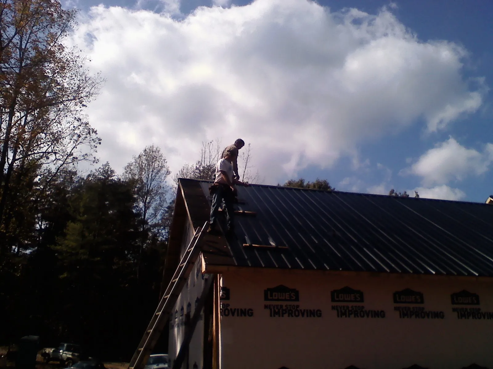 Roofer fastening dark metal panels high against a cloudy sky, from a Roof Inspection job in Nelsonia