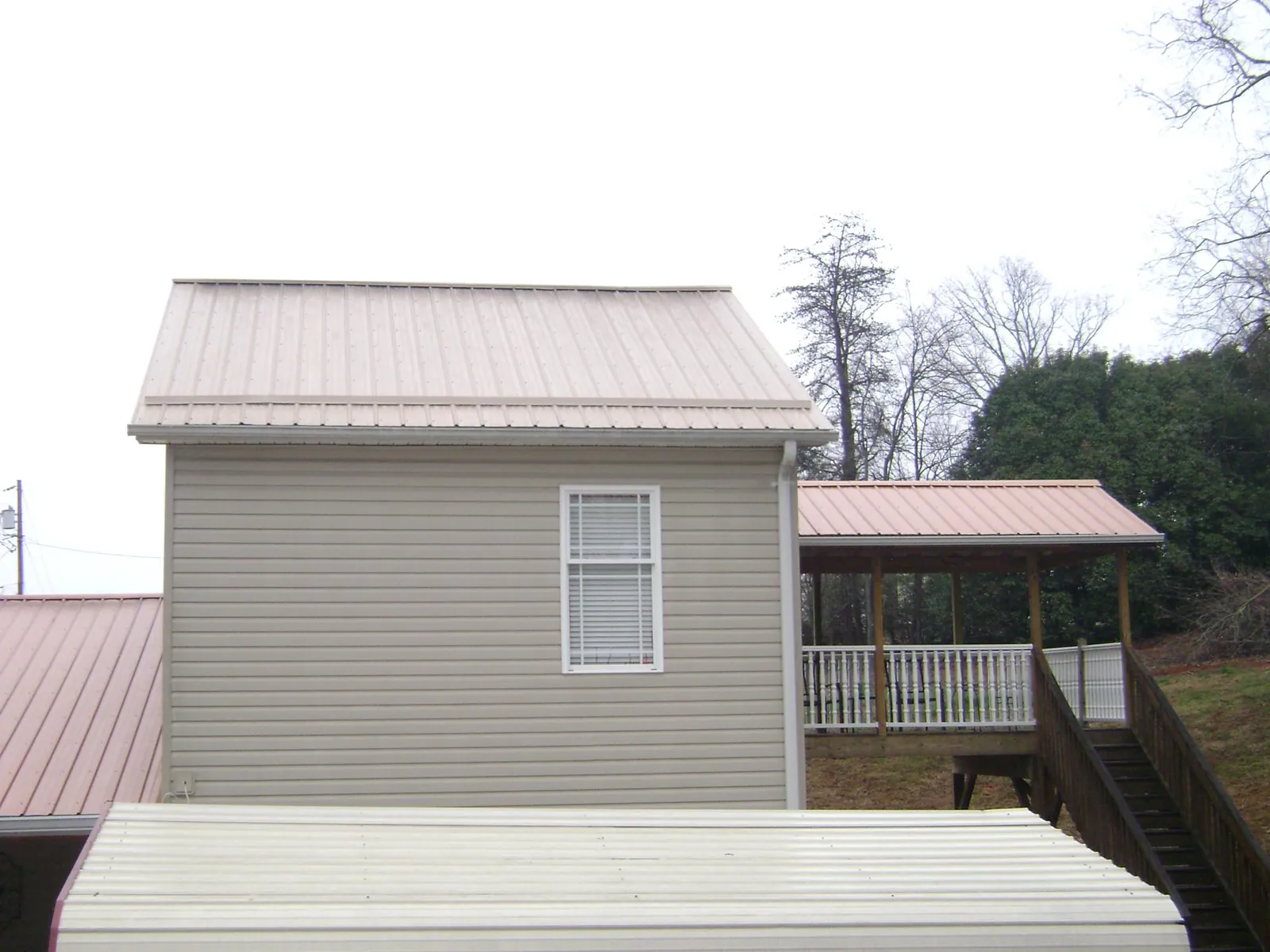 Tan metal roofs on a two story addition and attached porch, from a Roof Replacement job in Nelsonia